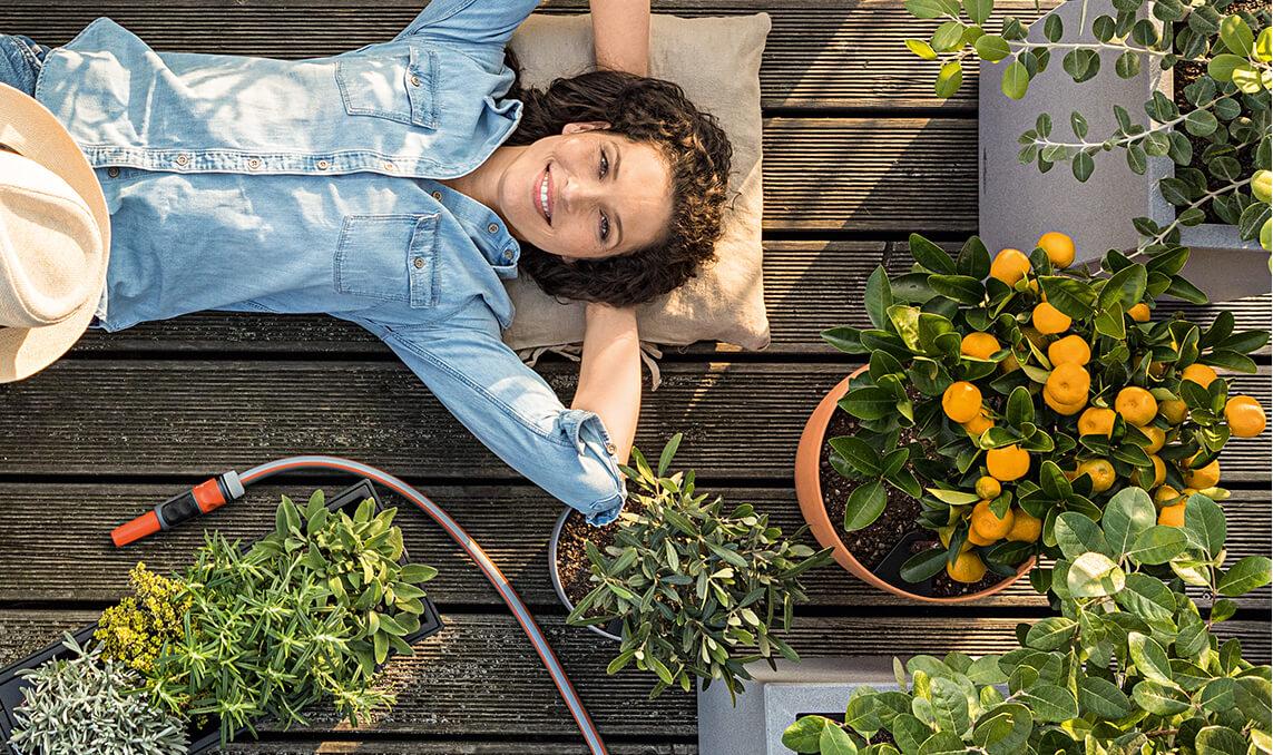 Frau liegt auf Terrasse zwischen LECHUZA Pflanzgefäßen
