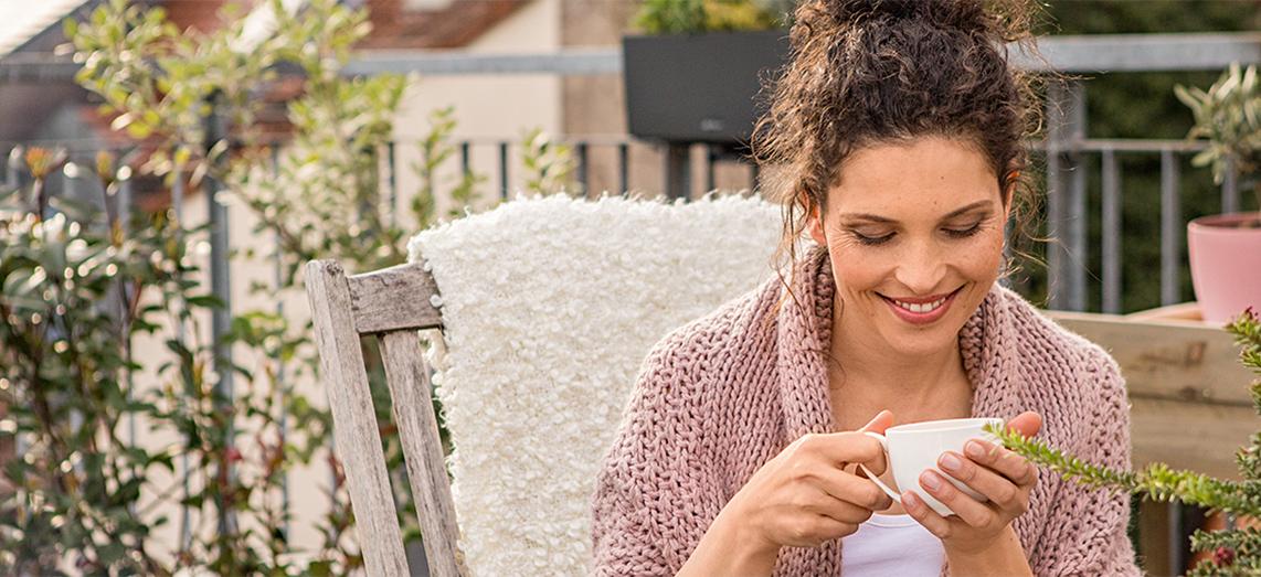 Frau sitzt auf Terrasse und trinkt Tee