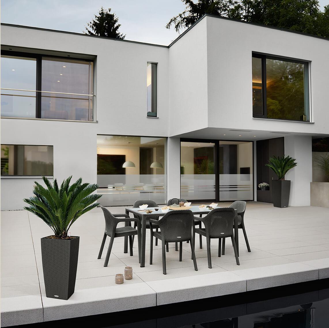 Modern Bauhaus villa at dusk. On the terrace in front of the villa there is a LECHUZA 7-seater suite in the colour granite