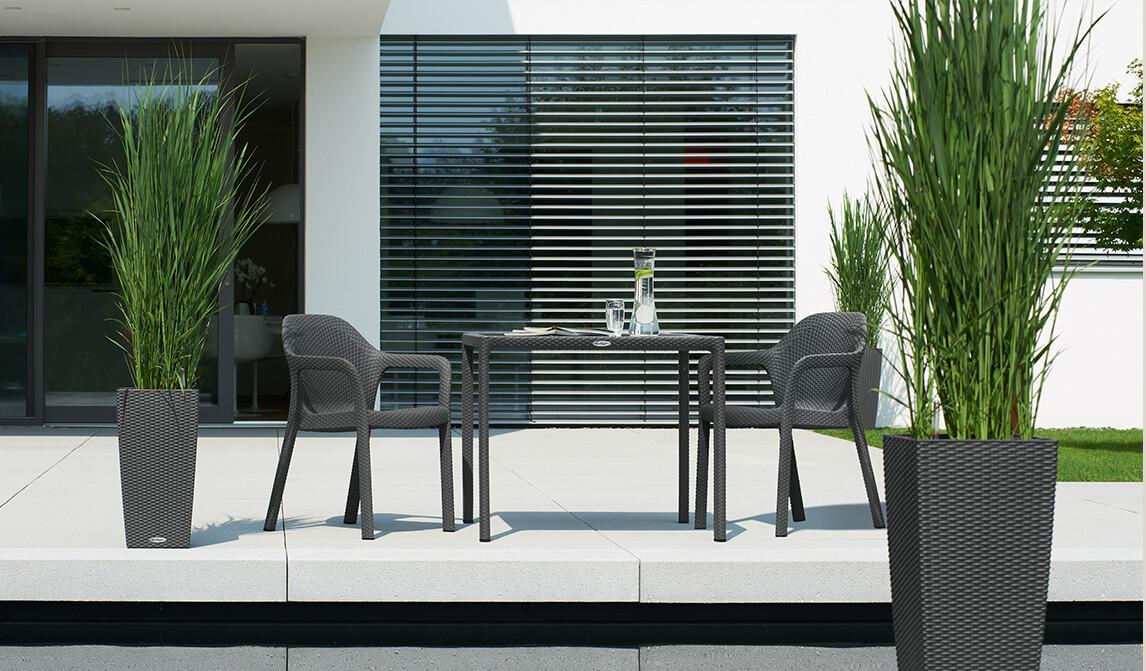 LECHUZA Gartentisch mit zwei Stühlen auf einer modernen Terrasse. Daneben LECHUZA Pflanzgefäße mit Bambus.