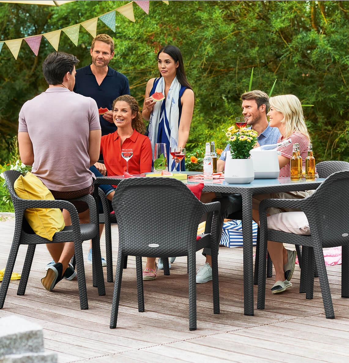 Freunde feiern eine Party im Garten und sitzen gemütlich an einem Tisch