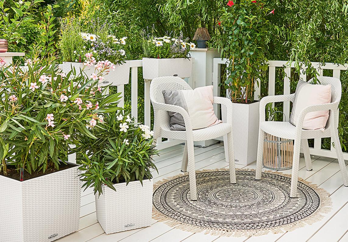 'Twee witte LECHUZA stapelstoelen op een romantisch landhuisterras. Daarnaast LECHUZA Cottage plantenbakken