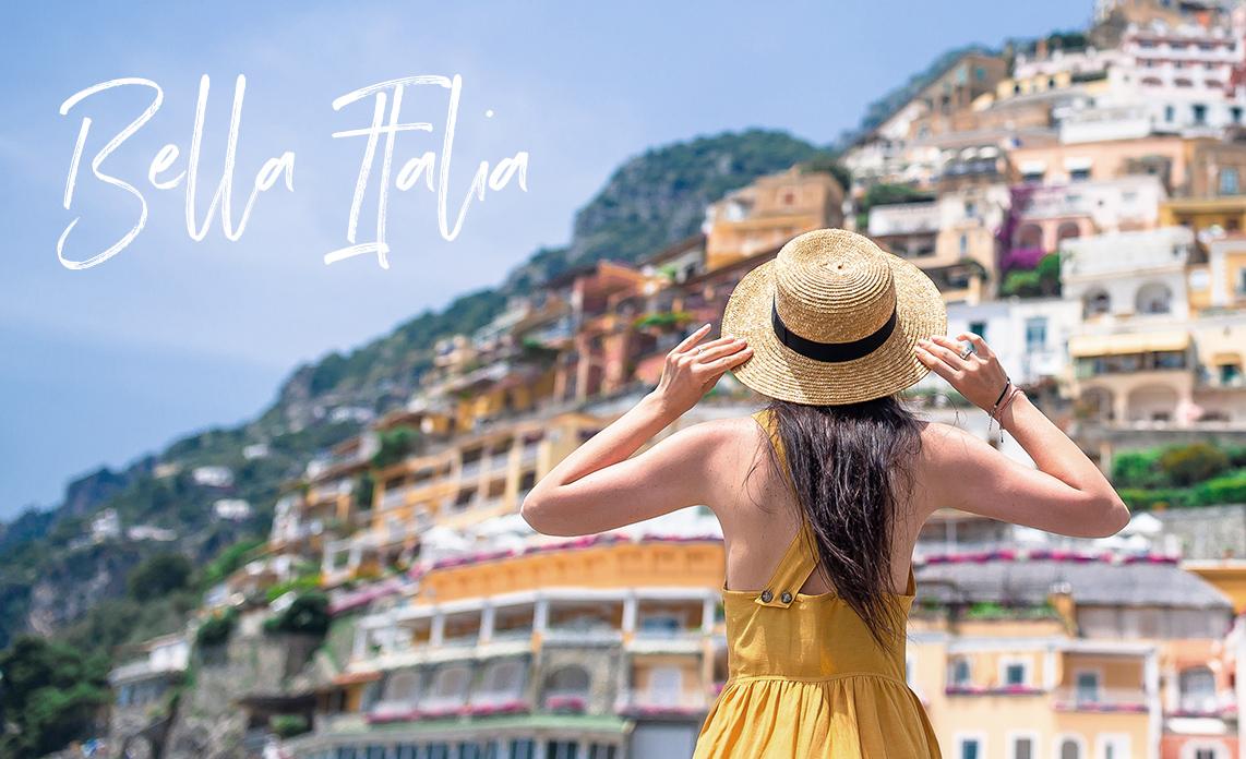 Junge Frau mit Strohhut und gelbem Kleid mit dem Dorf Positano (Amalfi Küste) im Hintergrund