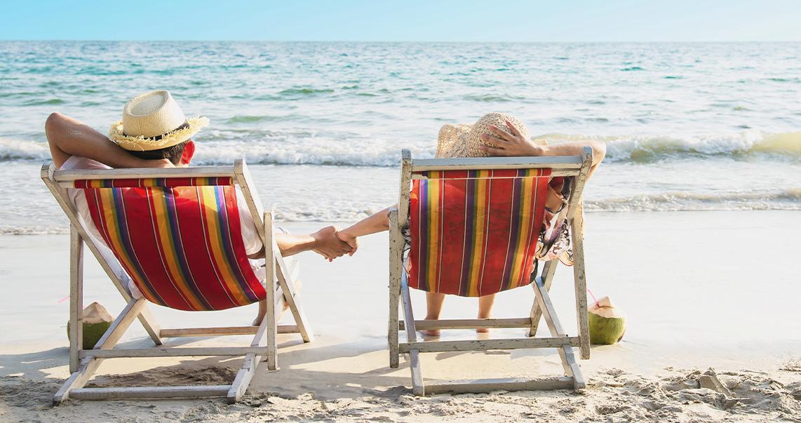 Entspanntes Paar liegt am Strand auf Liegestühlen und hält sich an der Hand