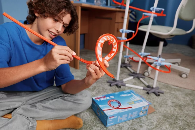 Junge sitzt im Kinderzimmer und verbindet zwei Schienenteile aus dem SKY TRAILS Looping Set