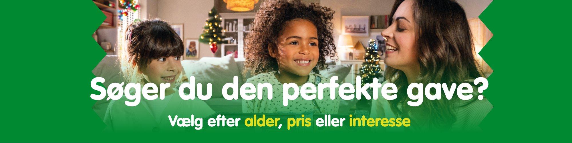 Zwei Kinder und eine Frau sitzen l&auml;chelnd vor einem weihnachtlich geschm&uuml;ckten Wohnzimmer mit Tannenbaum &ndash; perfekte Geschenkideen f&uuml;r Kinder entdecken.